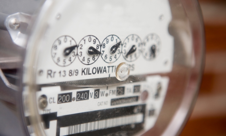 Close-up of an analog electric meter showing kilowatt-hour readings and voltage details through a clear cover.
